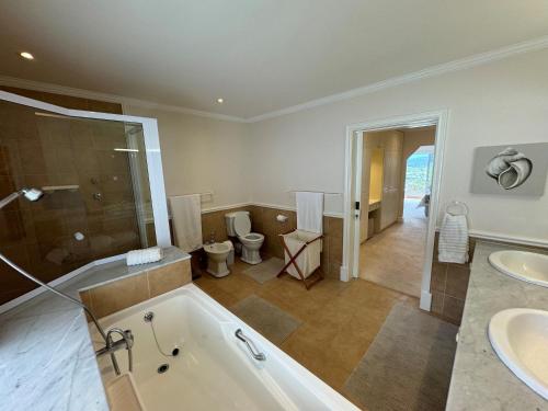 baño con 2 lavabos, bañera y 2 aseos en Holiday Villa with stunning views near beach., en Plettenberg Bay