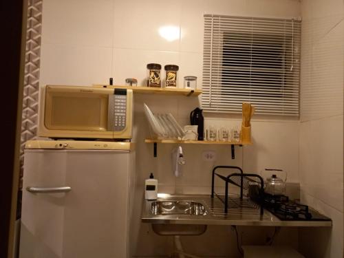 una pequeña cocina con microondas y fregadero en Suíte Studio 3 Enseada Tortuga Mobiliada en Guarujá