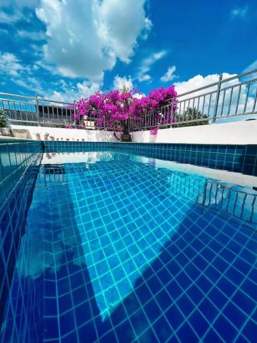 a blue swimming pool with blue water and purple flowers at Mammoth Art Studio Pool villa in old city in Chiang Mai