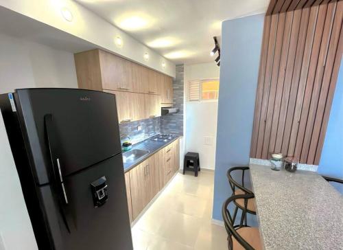 a kitchen with a black refrigerator and wooden cabinets at Apartamento con vista a las montañas, cerca Centro Comercial Mayales in Valledupar