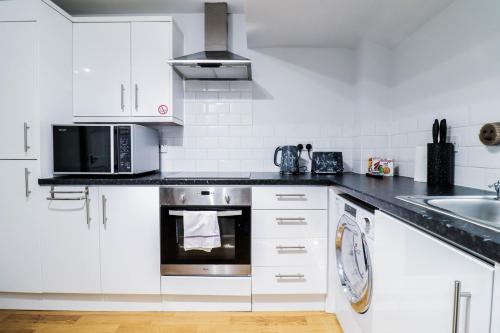a white kitchen with a microwave and a sink at 2 Bedroom Flat - Close to BBC studios! in Borehamwood