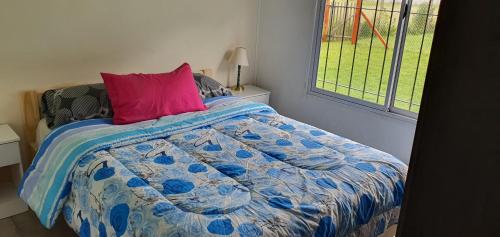 a bed with a blue comforter and a pink pillow at Casa con PILETA, PARRILLA y cochera cubierta in Chascomús
