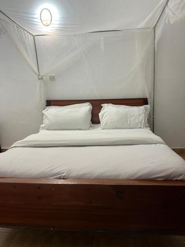 Cama con dosel con sábanas y almohadas blancas en J's Hotel & Accomodation, en Nakuru