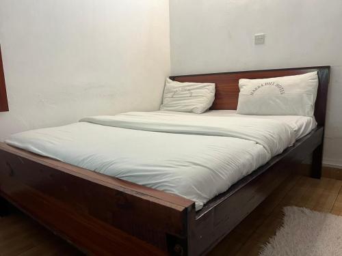 una cama de madera con sábanas blancas y almohadas. en J's Hotel & Accomodation, en Nakuru