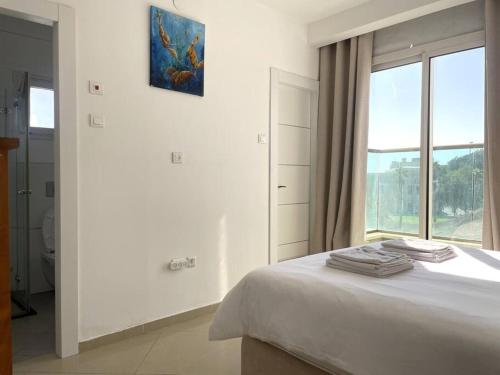 a white bedroom with a bed and a window at Sunny 3BR Apartment Golf Residence in Eilat
