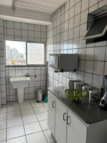 a white tiled kitchen with a sink and a microwave at Apartamento de 3 quartos na Praia da Fonte Guarapari in Guarapari