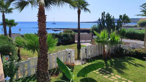 a white fence with palm trees and the ocean at Cuore di Ognina - Appartamenti vista mare in Ognina