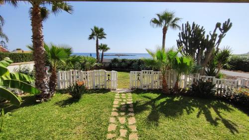a white fence in a yard with palm trees and the ocean at Cuore di Ognina - Appartamenti vista mare in Ognina