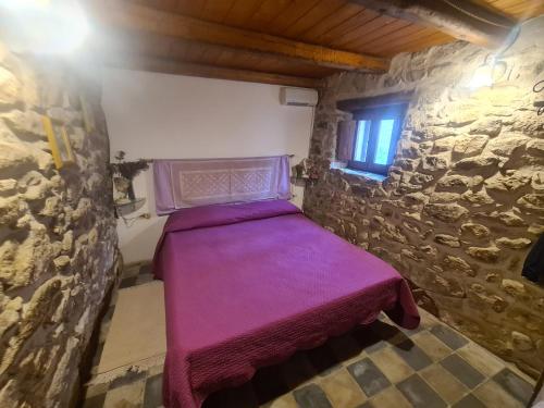 Habitación pequeña con cama morada en una pared de piedra. en Casa di Pietra, en Usellus