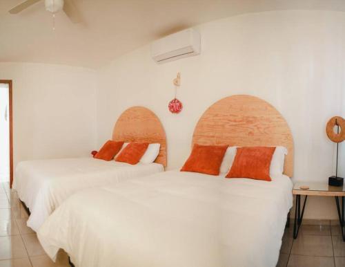 2 bedden in een kamer met witte lakens en oranje kussens bij Casa Amma - Amma in Matehuala
