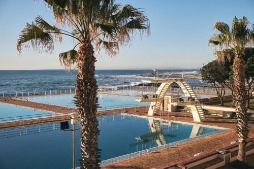 a palm tree next to a swimming pool next to the ocean at One26 On M Luxury serviced apartments - By Elevate in Cape Town
