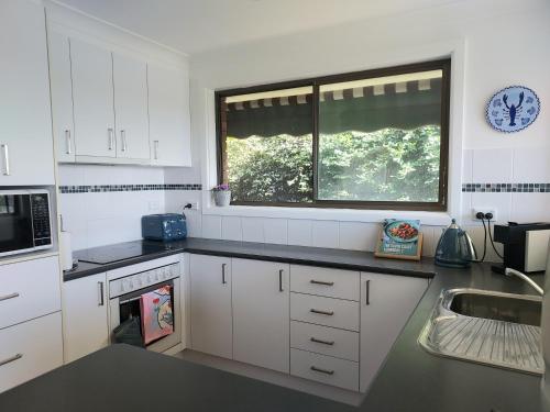 a kitchen with white cabinets and a sink and a window at Bondi Breeze @ Tuross Head in Tuross Heads