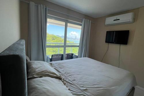 um quarto com uma cama e uma grande janela em Apto no terraço da rainha com vista para roda gigante e mar em Balneário Camboriú