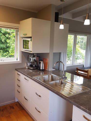 a kitchen with white cabinets and a sink and two windows at Perfect Lakeside Summer House in Rotorua