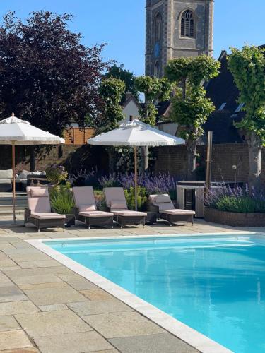 een zwembad met stoelen en parasols naast een gebouw bij The Pool House in Henley on Thames