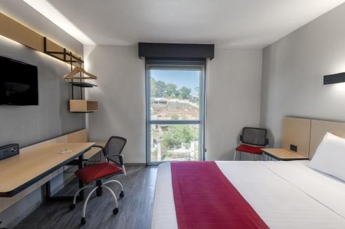 a hotel room with a bed and a desk and a window at City Express by Marriott Guadalajara Aeropuerto in Guadalajara