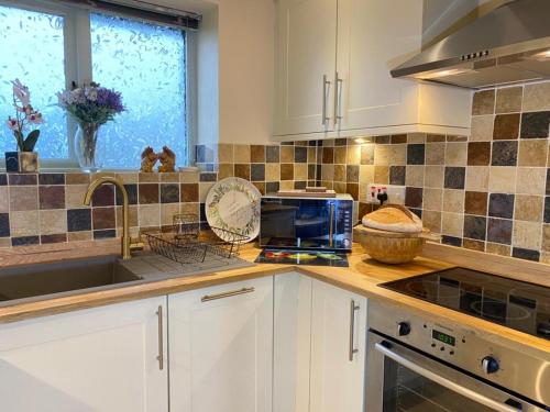 a kitchen with white cabinets and a sink and a window at Lune Cottage nestled between Lake District and Yorkshire Dales in Tebay