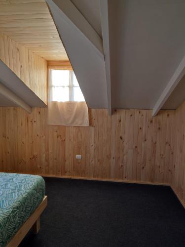 a bedroom with wooden walls and a window and a bed at Verdeagua Hostal in Chaitén