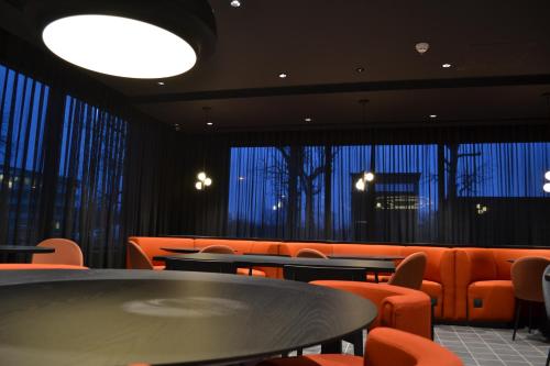 een eetkamer met oranje stoelen en tafels en ramen bij TRIBE Milano Malpensa in Vizzola Ticino