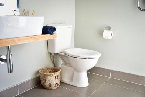 a bathroom with a toilet and a sink and a basket at Getaway Bach Whangapoua in Coromandel Town