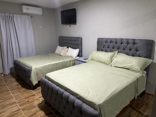 1 dormitorio con 2 camas y TV en la pared en Aparta Hotel Esa Buya en San Fernando de Monte Cristi