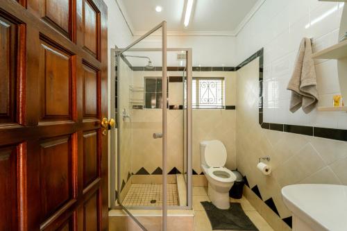 a bathroom with a toilet and a glass shower stall at Room in Villa - Zambezi Family Lodge - Leopard Room in Victoria Falls