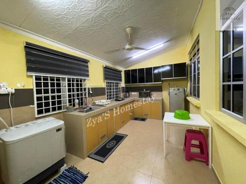 a large kitchen with yellow cabinets and a white table at Zya'S Homestay Gong Badak in Kampong Bukit Berangan