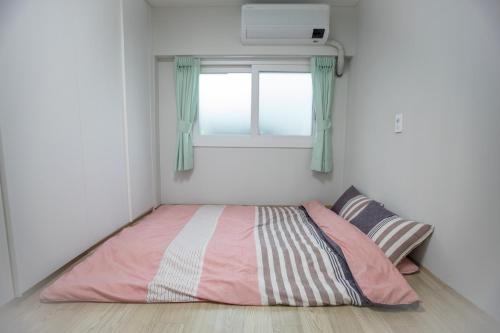 Cama en habitación pequeña con ventana en Hospitable House, en Seogwipo