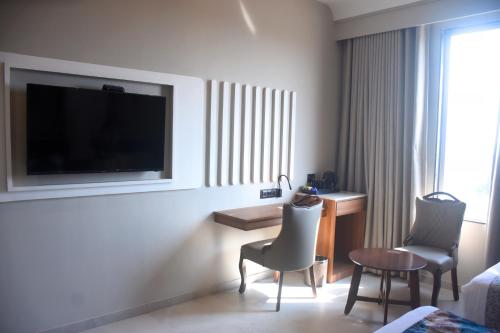a hotel room with a tv and a desk and chairs at Regenta Inn Motikhavdi Jamnagar in Jamnagar