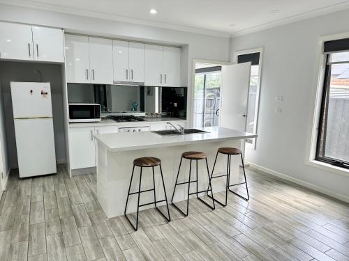een keuken met witte kasten, een aanrecht en krukken bij Townhouse in West Footscray in Seddon