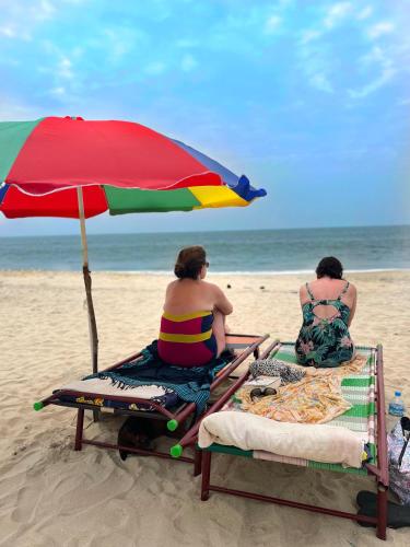 two women sitting on the beach under an umbrella at Marari Anandu Beach Villa in Mararikulam