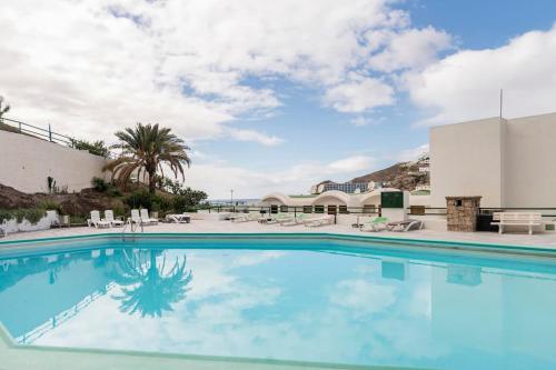 a large swimming pool with chairs and a building at 1005 Ocean view house La cascada in Puerto Rico de Gran Canaria