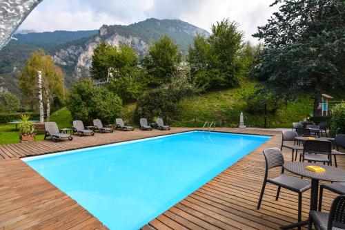 a swimming pool on a wooden deck with chairs and a mountain at Hotel Cima d'Oro in Ledro