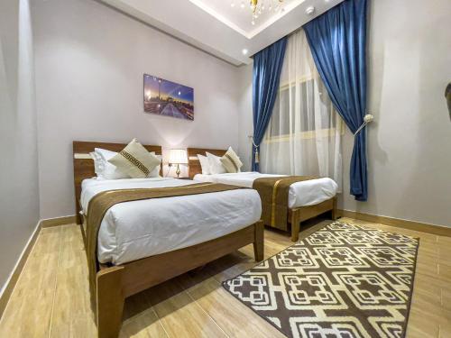 two beds in a room with blue curtains and a rug at Landmark Hotel Suites in Tabuk