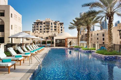 einen Pool mit Stühlen, Palmen und Gebäuden in der Unterkunft The Heritage Hotel, Autograph Collection in Dubai