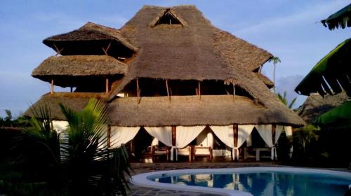 un complejo con un edificio con techo de paja y una piscina en Piano B suites, en Watamu