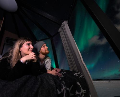 a man and a woman sitting in a tent watching the northern lights at Aurora Nest – Eco Glass Igloo in Rovaniemi