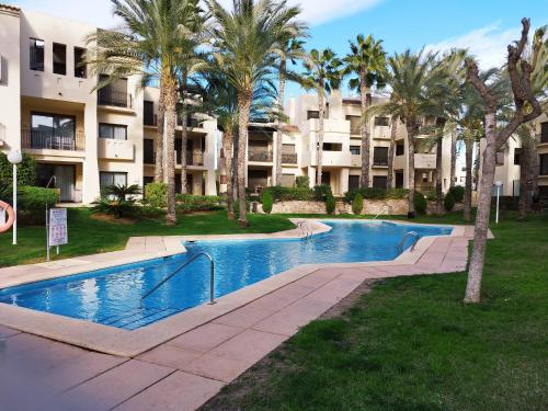 a swimming pool with palm trees in front of a building at Apartamento 3 dormitorios Roda Golf in Murcia