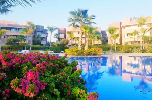 a resort swimming pool with pink flowers and palm trees at Luxurious Stay at Prestigia Golf Marrakech with Golf Course, Pool, and Breathtaking Atlas Mountains View in Marrakech