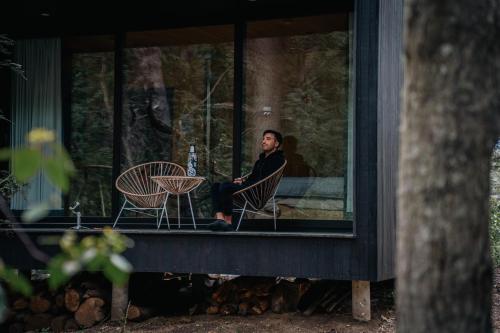 un hombre sentado en una silla en el porche de una casa en El Bosque en San Carlos de Bariloche