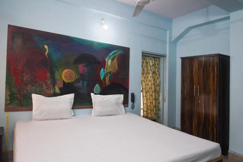 a bedroom with a large white bed with a painting on the wall at OYO Blue Cherry Guest House in Ballygunge