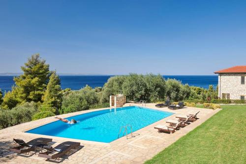 a person swimming in a pool with chairs and the ocean at Infinity blue villa in Nikiti