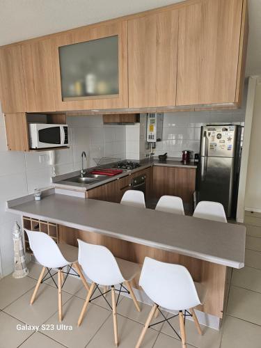 a kitchen with a counter and white chairs in it at Depto Parque Mar El Tabo in El Tabo