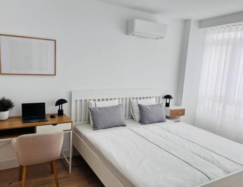 a white bedroom with a bed with a desk and a laptop at Arandas in Granada