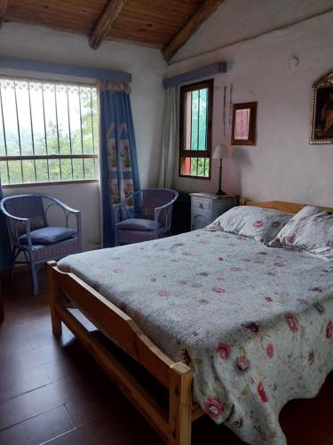 a bedroom with a bed and two chairs and windows at Casa de campo en tafi del valle in San Miguel de Tucumán