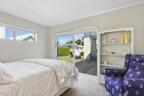 a white bedroom with a bed and a blue chair at Estuary Bliss Getaway in Mangawhai