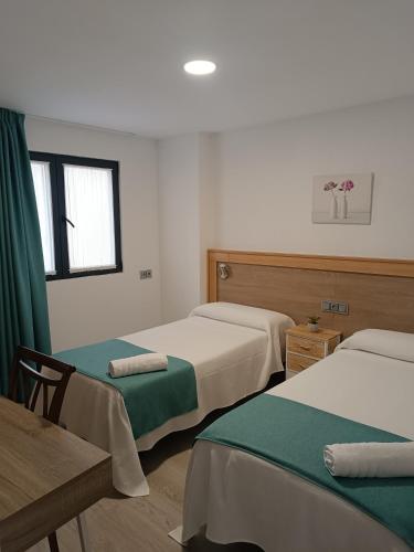 Zimmer mit 3 Betten, einem Tisch und einem Fenster in der Unterkunft Apartamentos turisticos Ávila Puerta de San Isidro 1-4 in Avila