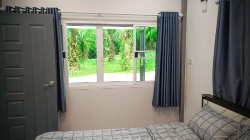 a bedroom with a window with blue curtains and a bed at The Engineer's Villas, Krabi in Ban Khlong Chi Lat