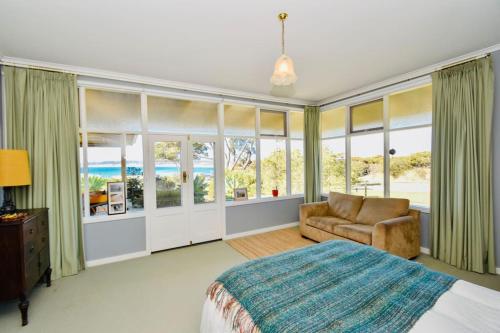 a bedroom with a bed and a couch and windows at The Old School House in Emu Bay