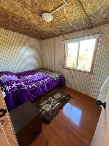 a small bedroom with a purple bed and a window at Los avellanos in Chonchi